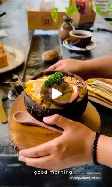 Hands holding a coconut-shell smoothie bowl topped with mango, passion fruit and coconut flakes
