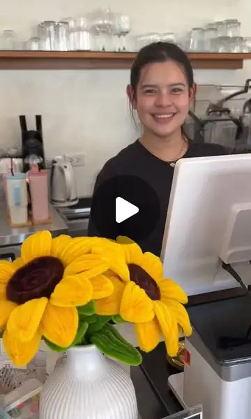 Smiling barista behind the counter with a bouquet of sunflowers in front