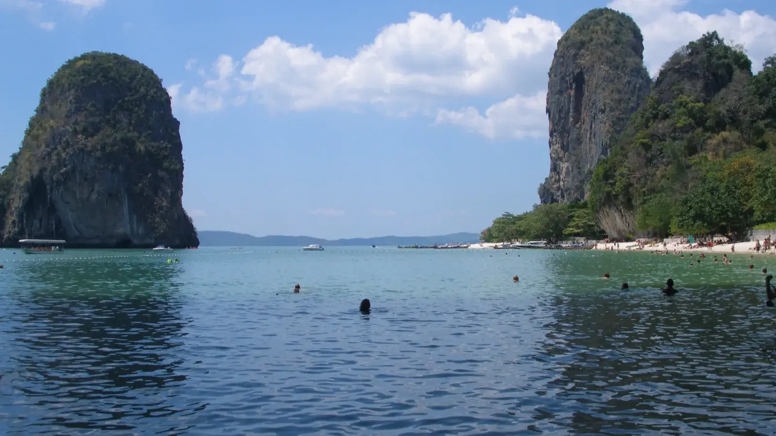 Calm turquoise water and a quiet sandy beach framed by dramatic limestone cliffs under a clear sky in Krabi