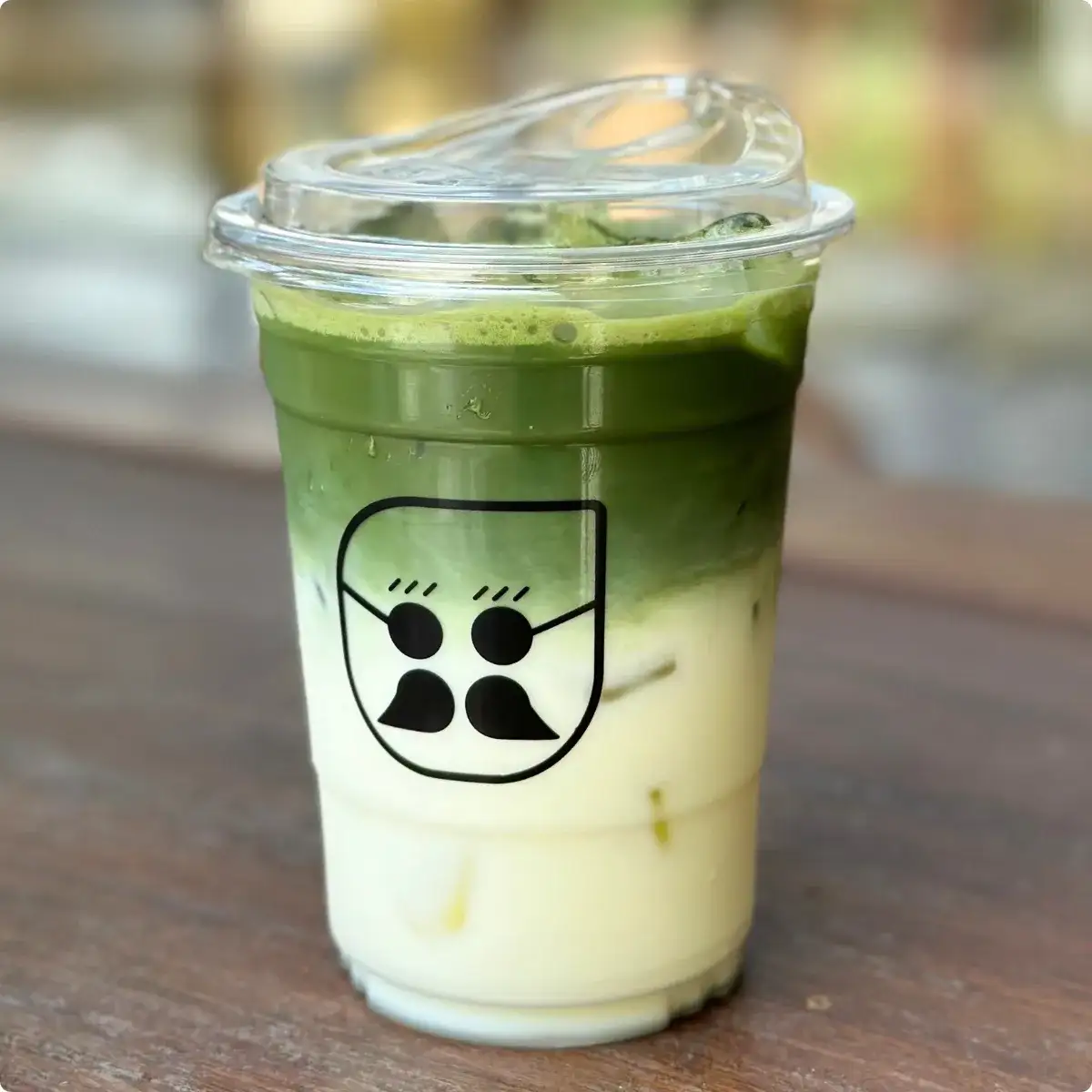 A bowl of vivid jade-green matcha being whisked with a bamboo chasen beside a small pile of bright matcha powder on a cafe counter