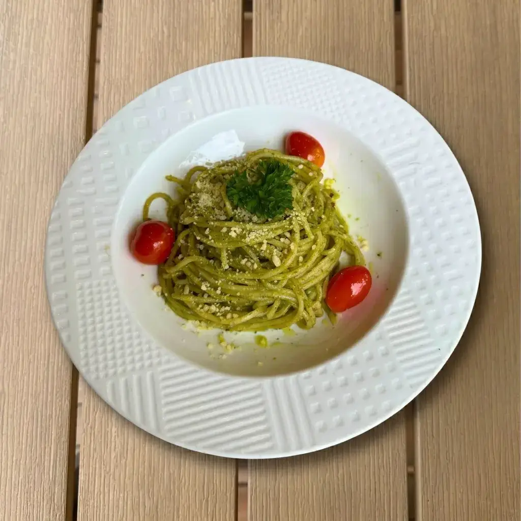 Spaghetti pesto with tomato and grated parmesan in a white bowl on a warm wooden table
