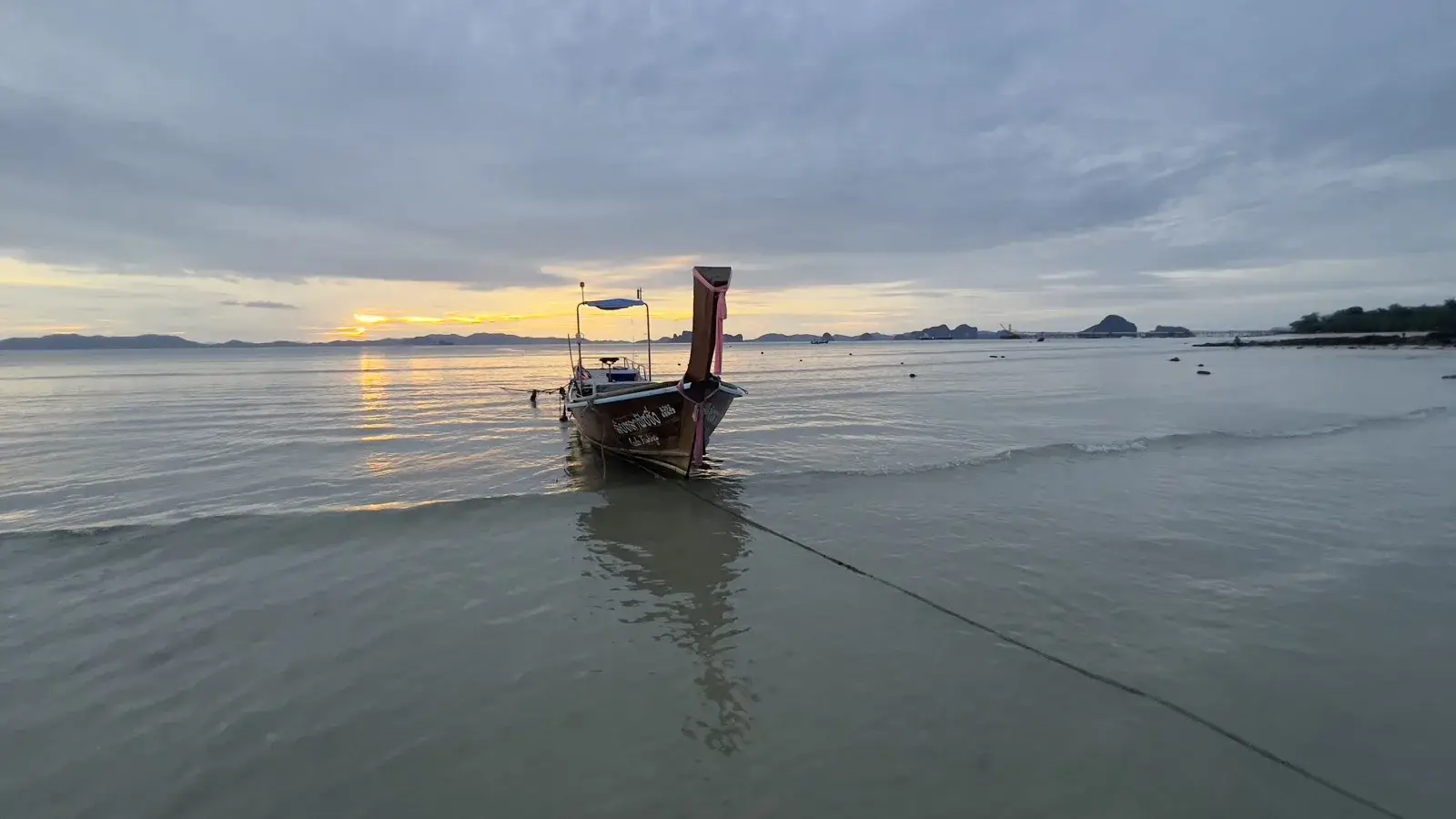 A near-empty stretch of calm shallow water at a Krabi beach at golden hour, with a limestone headland rising at the far end
