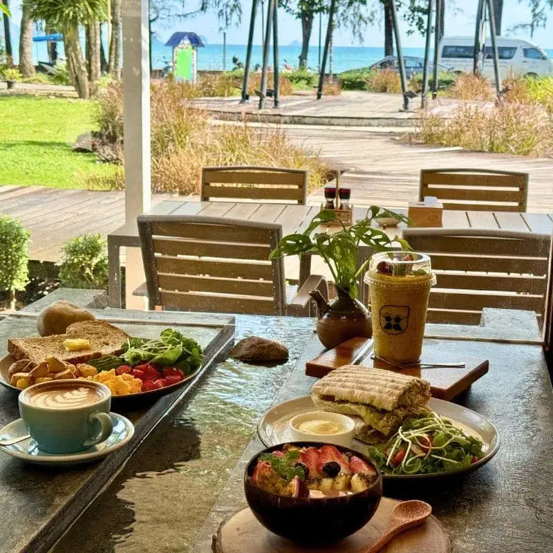 Brunch spread with breakfast set, smoothie bowl and latte on the water table, sea view behind