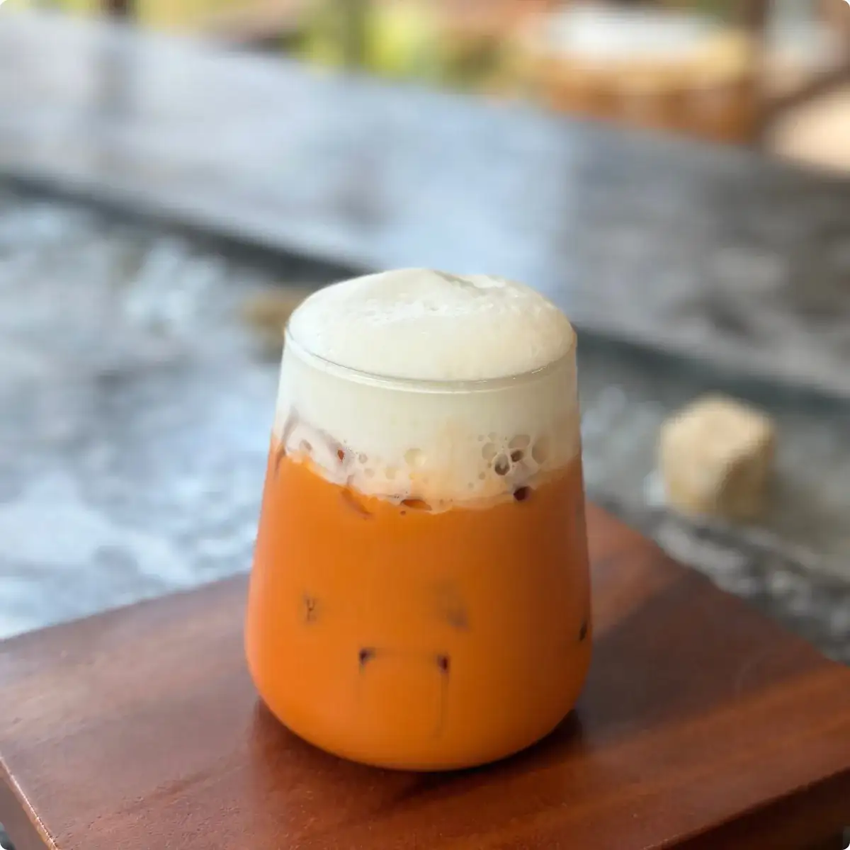Three tall glasses of Thai iced drinks on a cafe table — black oliang, milky kafae yen, and bright-orange cha yen — beaded with condensation over ice