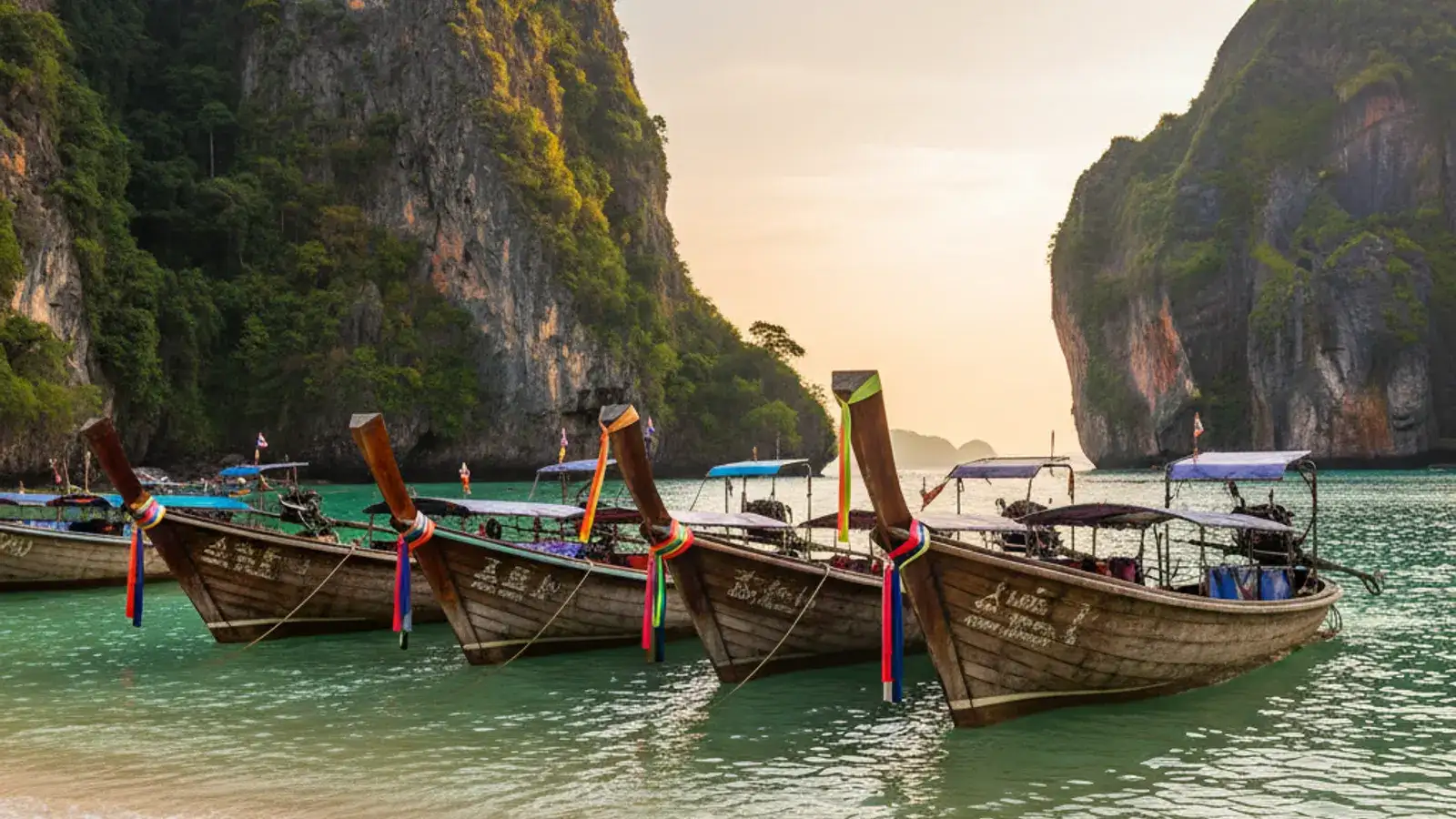 Longtail boats moored on Ao Nang Beach at golden hour, with limestone cliffs rising behind the bay