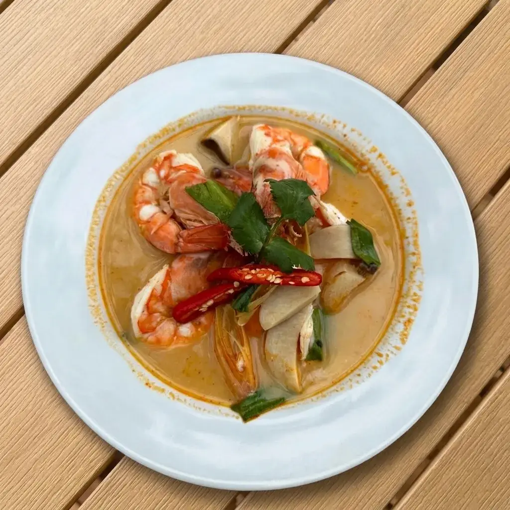 A bowl of tom yum kung — clear-red hot-and-sour prawn soup — with lemongrass and lime
