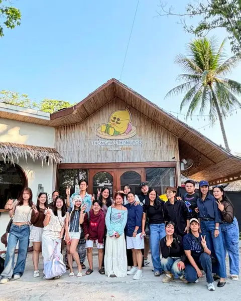 The whole Thongyib Thongyod team posing in front of the bamboo shopfront under the mascot sign