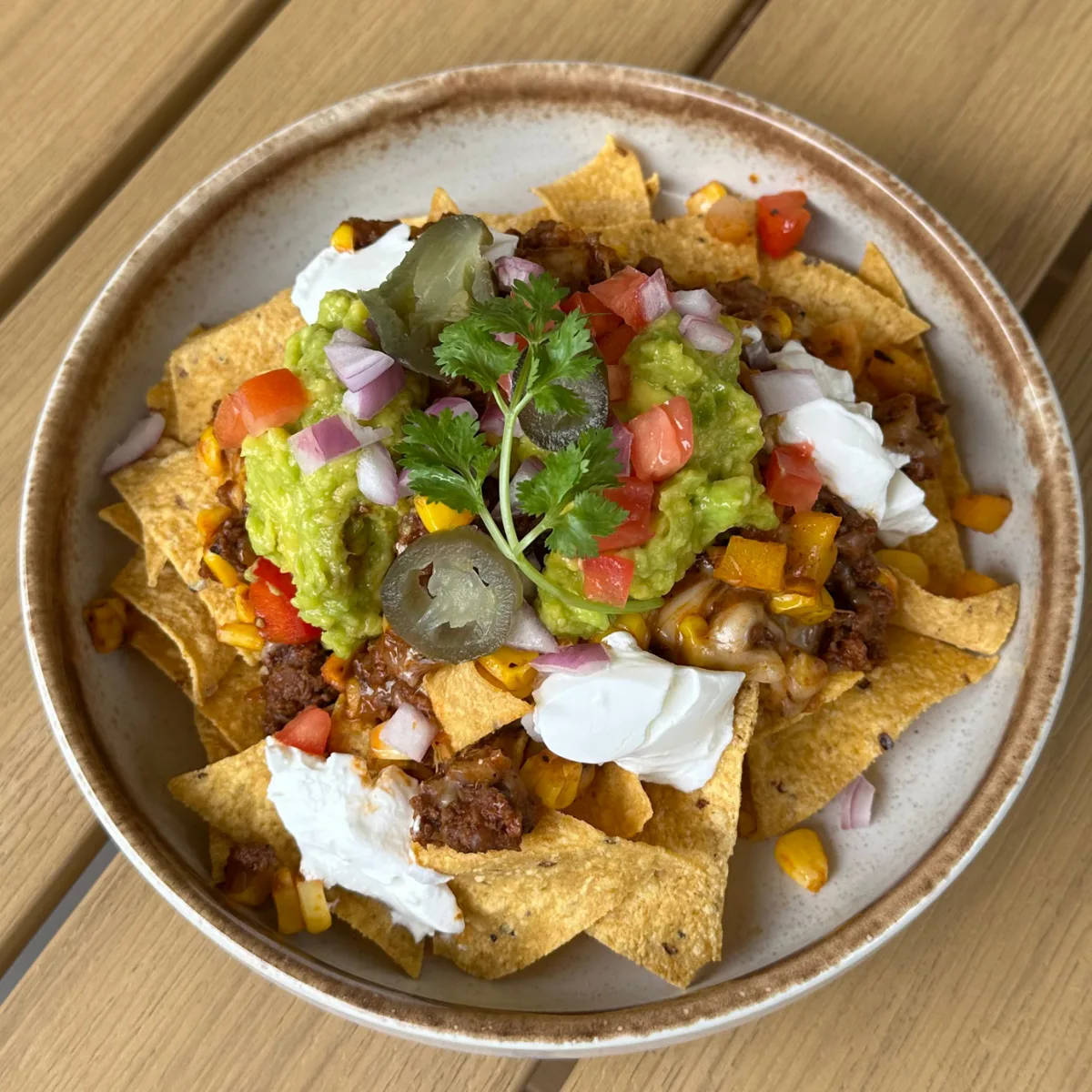 A loaded plate of nachos topped with guacamole, sour cream, jalapeños, diced tomato and red onion