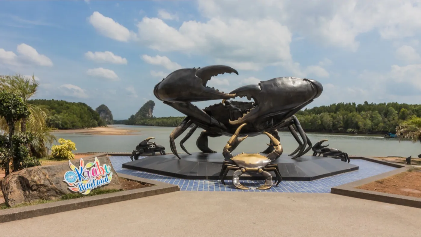 A large black-crab sculpture on the Krabi riverfront, mangroves and a limestone hill across the water behind it