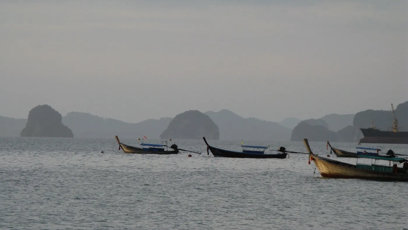 Longtail boats moored on the calm water off Klong Muang Beach, with scattered limestone islets across the bay