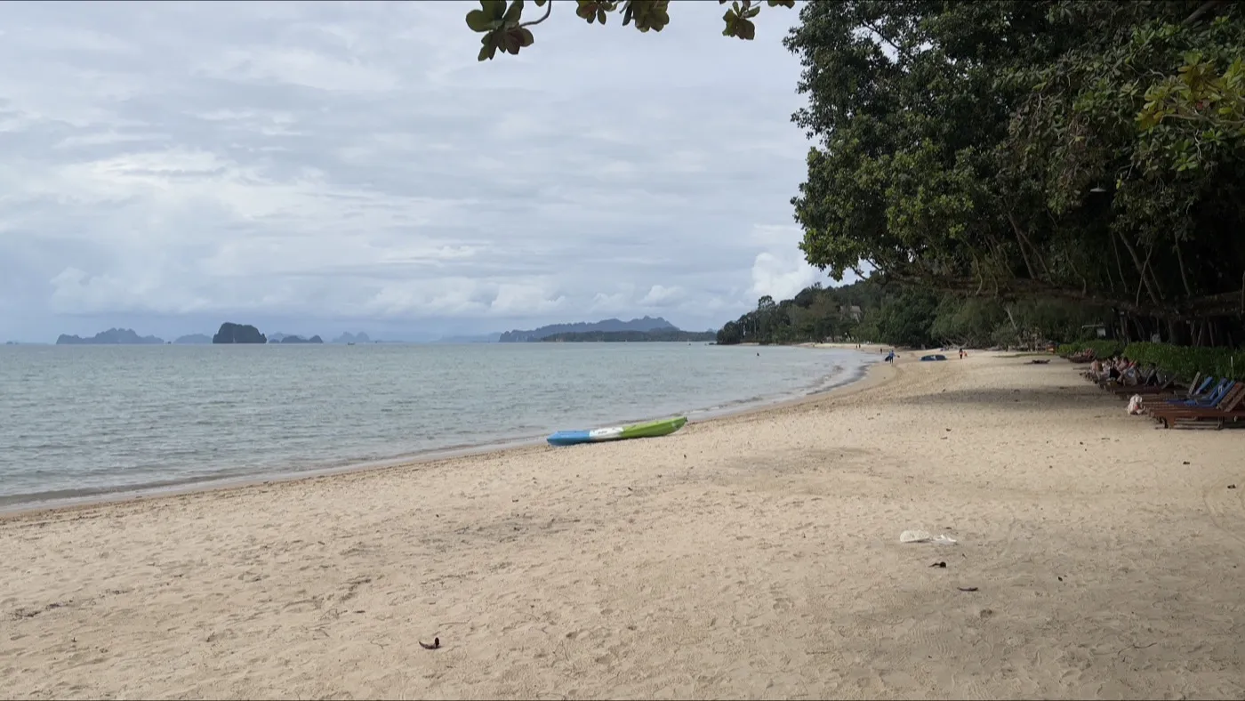 The quiet sand and calm water of Tubkaek Beach, framed by trees, with limestone islands across the bay