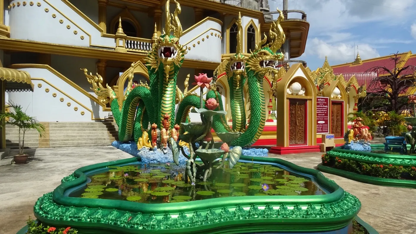 A colourful green naga serpent fountain in the courtyard of the lower Tiger Cave Temple complex, gold-trimmed shrine buildings behind